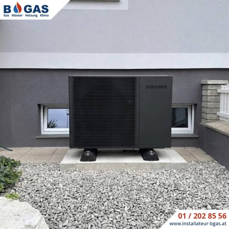Frontalansicht einer anthrazitfarbenen Samsung Mono HT Luft-Wasser-Wärmepumpe, die auf schallentkoppelten Big-Foot-Dämpfern und einem Betonfundament vor einer Hausfassade montiert ist.