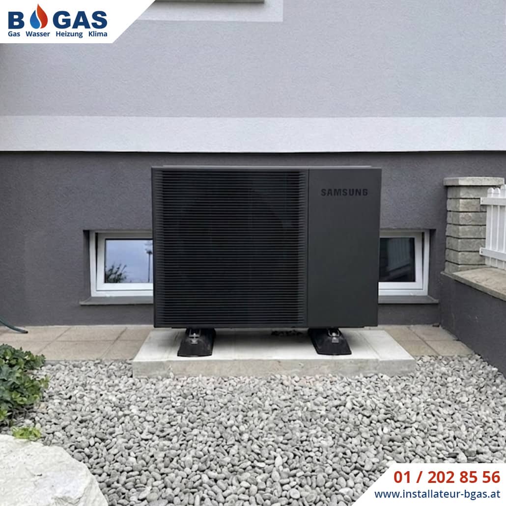 Frontalansicht einer anthrazitfarbenen Samsung Mono HT Luft-Wasser-Wärmepumpe, die auf schallentkoppelten Big-Foot-Dämpfern und einem Betonfundament vor einer Hausfassade montiert ist.